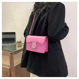 Pink leather crossbody bag with wavy flap and silver U-shaped clasp on a black blazer