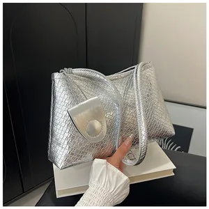 Detailed view of silver metallic shoulder bag with crocodile texture on a white book