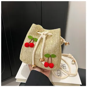 Detail of straw bucket bag with 3D cherry accents and cream drawstring closure