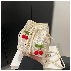 Detail of straw bucket bag with red pompom cherries and green leaves on ivory woven texture