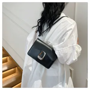 Detail of minimalist black leather crossbody bag with a large silver metallic buckle
