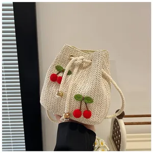Detail of hand-woven straw bucket bag featuring 3D cherry pom-poms and cotton rope strap