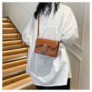 Brown leather crossbody square bag with metal buckle detail worn by model on white shirt