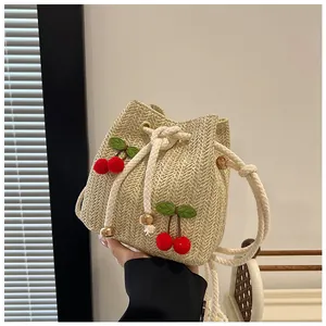 Detail of hand-woven straw bucket bag with red cherry accents and white cotton drawstrings
