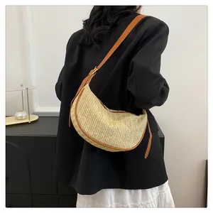 Detail of hand-woven straw crescent bag with brown PU leather trim and adjustable strap