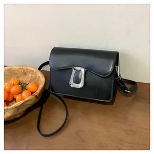 Detailed close-up of a minimalist black square crossbody bag with silver metal clasp