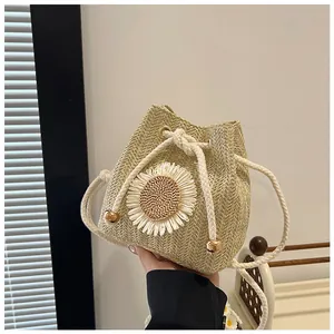 Detail of hand-woven beige straw bucket bag featuring a white 3D daisy flower and drawstring