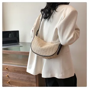 Close-up of beige woven crescent bag with dark brown leather straps on woman's shoulder