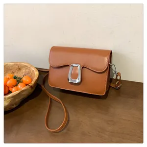 Brown leather crossbody bag with silver buckle on a wooden table with cherry tomatoes