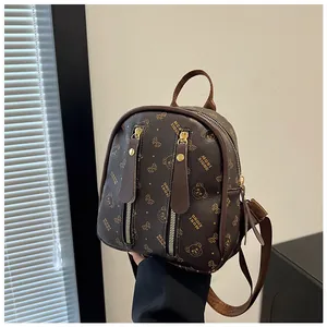 Detail of a mini brown leather backpack featuring golden bear monogram and metal zippers