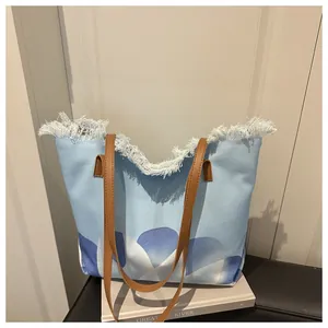 Detalle del bolso tote azul con estampado abstracto, flecos blancos y asas de cuero marrón