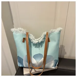 Detalle del bolso tote azul claro con bordes de flecos blancos y asas de cuero marrón