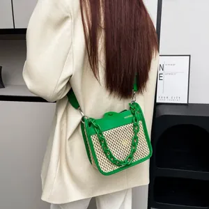 Detail view of woven straw crossbody bag with green chain and brand logo on model