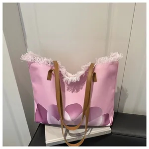 Detalle del bolso tote de lona rosa con estampado floral, bordes deshilachados y asas marrones