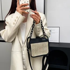 Detail of woven straw crossbody bag with black leather trim and chunky chain strap