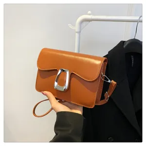 Detail of caramel crossbody bag featuring a wavy flap edge and silver D-ring metal buckle