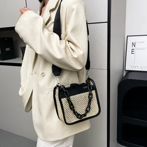 Detail of woven straw crossbody bag featuring black leather trim and decorative chain