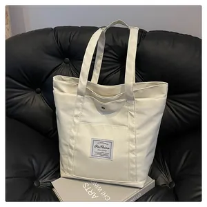 Detalle de bolso tote de nailon blanco roto con etiqueta de moda en sofá de cuero negro