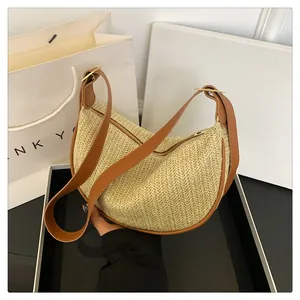 Detail of woven crescent bag featuring natural straw texture and brown leather trim accents