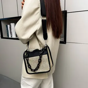 Detail of beige woven crossbody bag featuring black chain and contrast leather trim