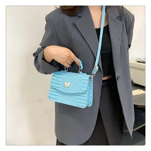 Close-up of light blue crocodile texture handbag with golden butterfly detail on model