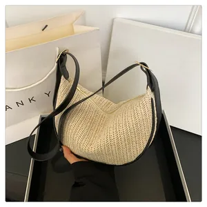 Close-up of beige woven crescent bag featuring black leather trim and gold metal zipper