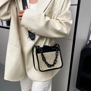 Close-up of woven straw crossbody bag with black leather trim and bold acrylic chain