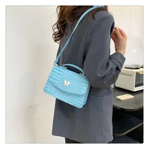 Detail of light blue crocodile texture handbag featuring a white butterfly ornament