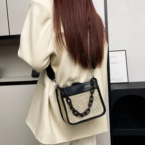 Close-up of woven straw crossbody bag with thick black chain and adjustable strap