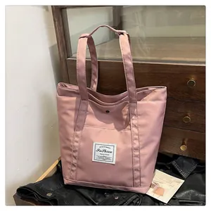 Detalle de bolsa tote de nailon rosa con bolsillo frontal y etiqueta en mesa de madera