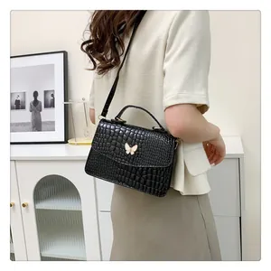 Close-up of black crocodile-embossed handbag featuring a white butterfly clasp in home setting