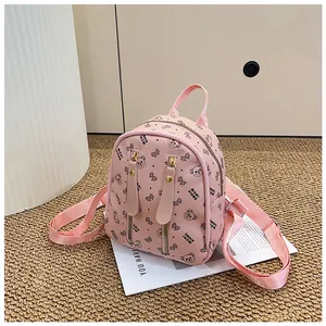 Close-up of pink mini backpack with bear pattern, gold zippers, and metal stud details