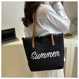 Dettaglio del ricamo Summer su una borsa tote in tela nera con finiture a nappe