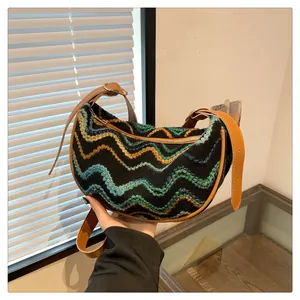 Detail of colorful woven knit wave pattern and brown leather strap on a crescent hobo bag