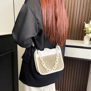 Close-up of woven straw handbag featuring white leather trim and chunky plastic chain link