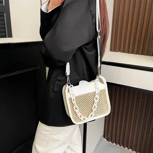 Close-up of woven straw crossbody bag with white leather trim and chunky chain detail