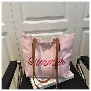 Dettaglio della borsa tote in tela rosa con ricamo Summer e bordi sfrangiati sulla sedia
