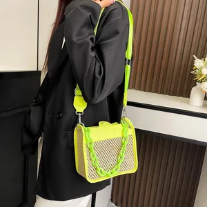 Detail of neon yellow woven crossbody bag with chunky plastic chain and textured leather trim