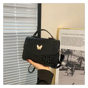 Close-up of black crocodile-embossed handbag featuring a gold-edged white butterfly detail