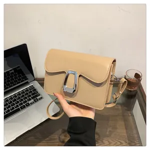 Detail of minimalist beige crossbody bag with silver buckle in a modern office setup