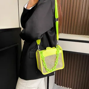 Green woven crossbody bag with thick chain handle worn by a model in black blazer