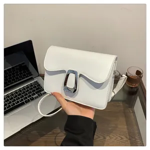 Close-up of a white square crossbody bag with wavy flap design and large silver U-buckle