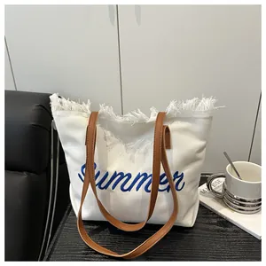 Dettaglio di una borsa tote in tela bianca con ricamo Summer blu e bordi con frange