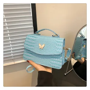 Close-up of light blue crocodile pattern handbag with white butterfly metal buckle detail
