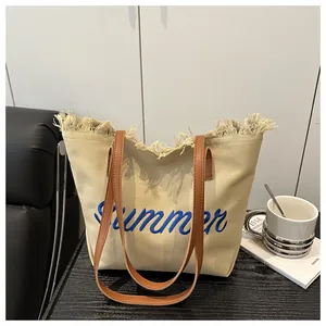 Dettaglio della borsa tote in tela beige con frange di paglia e ricamo blu Summer