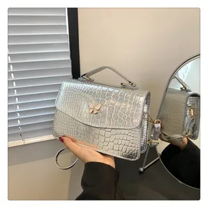 Detailed view of silver butterfly buckle on faux crocodile texture crossbody bag