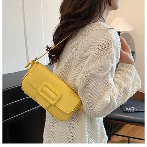 Detailed view of a bright yellow baguette shoulder bag worn over a white crochet sweater