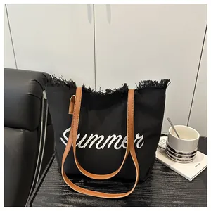 Dettaglio della borsa tote in tela nera con ricamo Summer bianco e bordi a frange