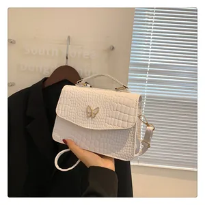 Detail of white crocodile texture bag featuring a gold butterfly buckle and shoulder strap