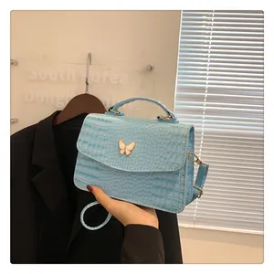 Detailed view of light blue crocodile texture bag with white butterfly metal accessory